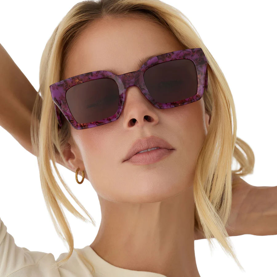 Woman wearing purple sunglasses with a tortoise pattern on a white background