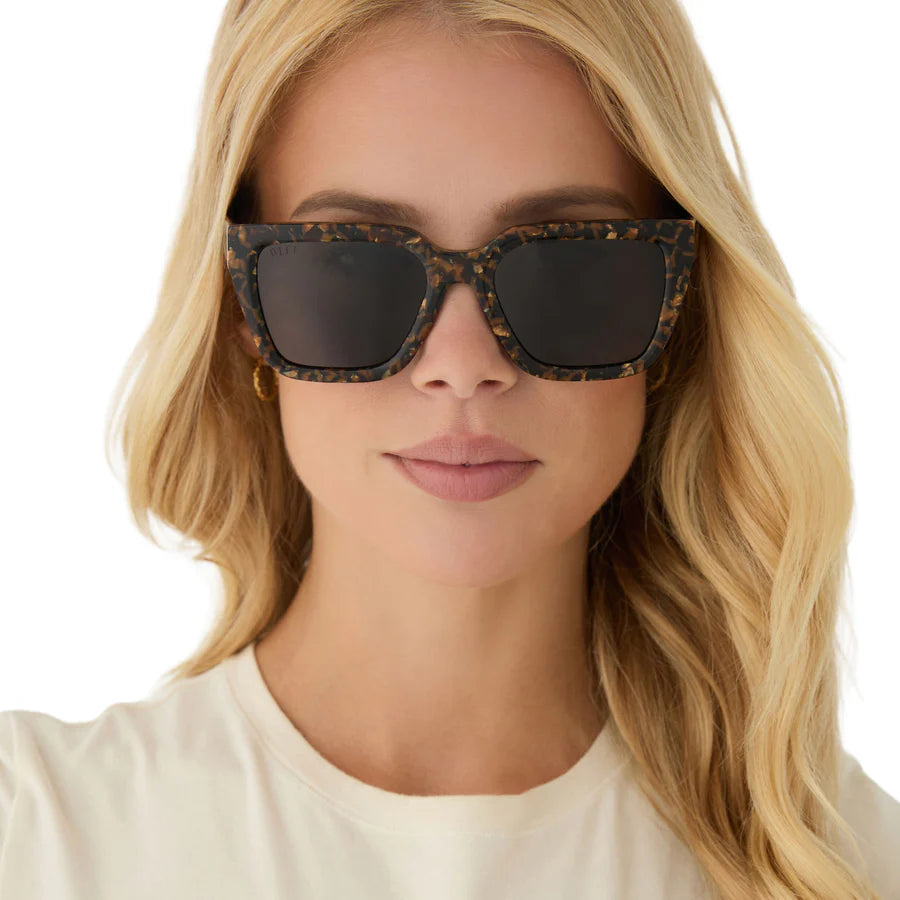Woman wearing tortoise print glitter sunglasses with a plain background
