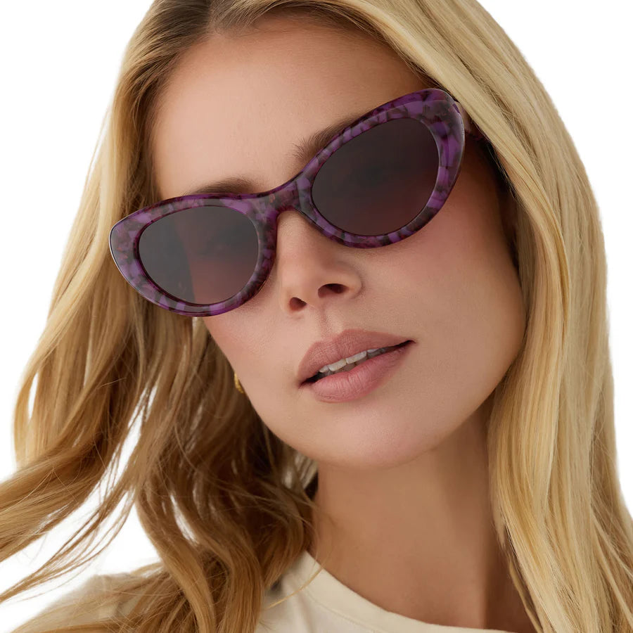 Woman wearing purple tortoise sunglasses with a white background