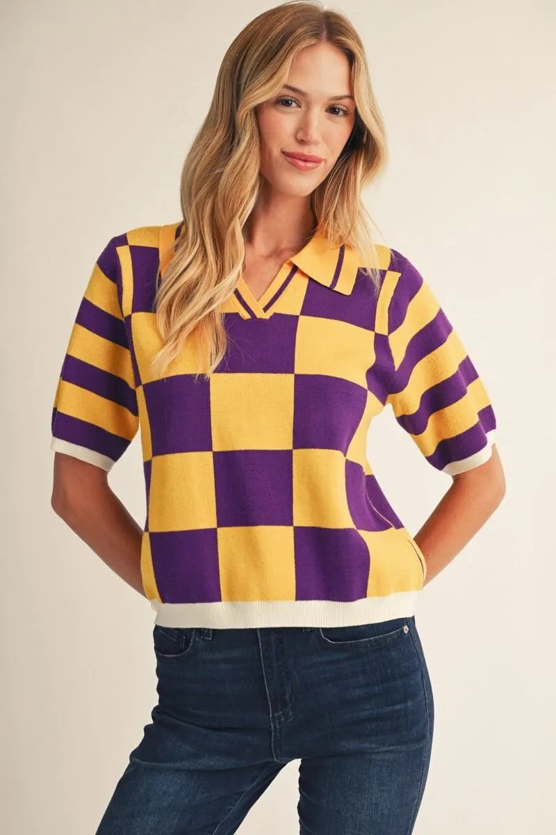 A woman wearing a short-sleeve knit polo shirt with a bold yellow and purple checkerboard pattern and white trim, paired with dark blue jeans, against a plain beige background.