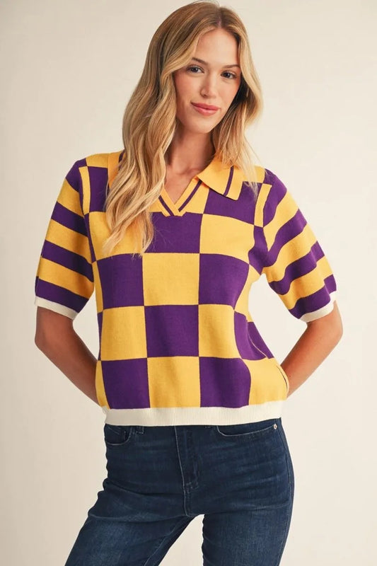 A woman wearing a short-sleeve knit polo shirt with a bold yellow and purple checkerboard pattern and white trim, paired with dark blue jeans, against a plain beige background.