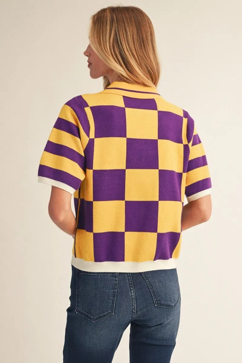 A woman shown from the back wearing a short-sleeve knit polo shirt with a bold yellow and purple checkerboard pattern and white trim, paired with blue jeans against a plain beige studio background.