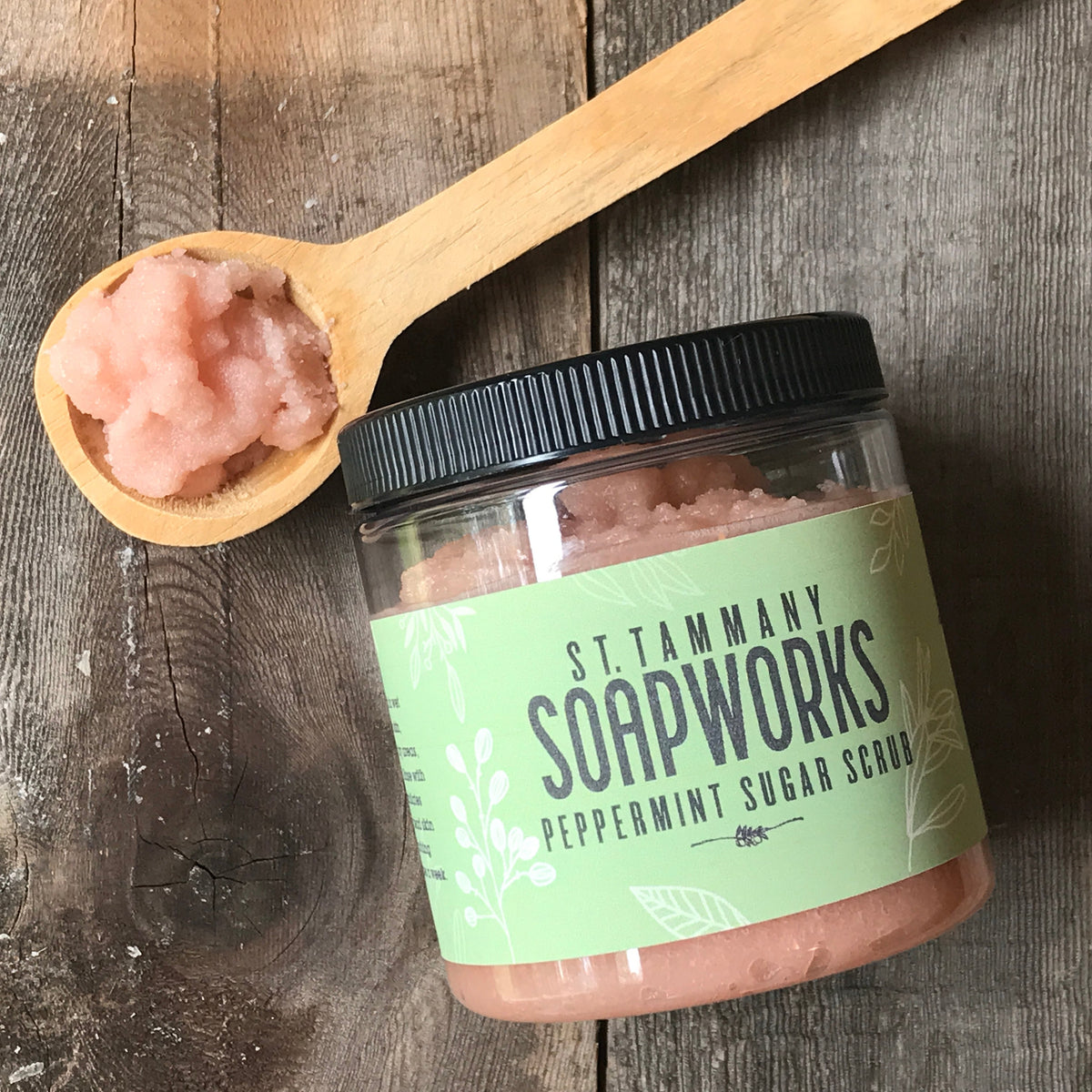 Open jar of pink Peppermint Sugar Scrub with a wooden spoon