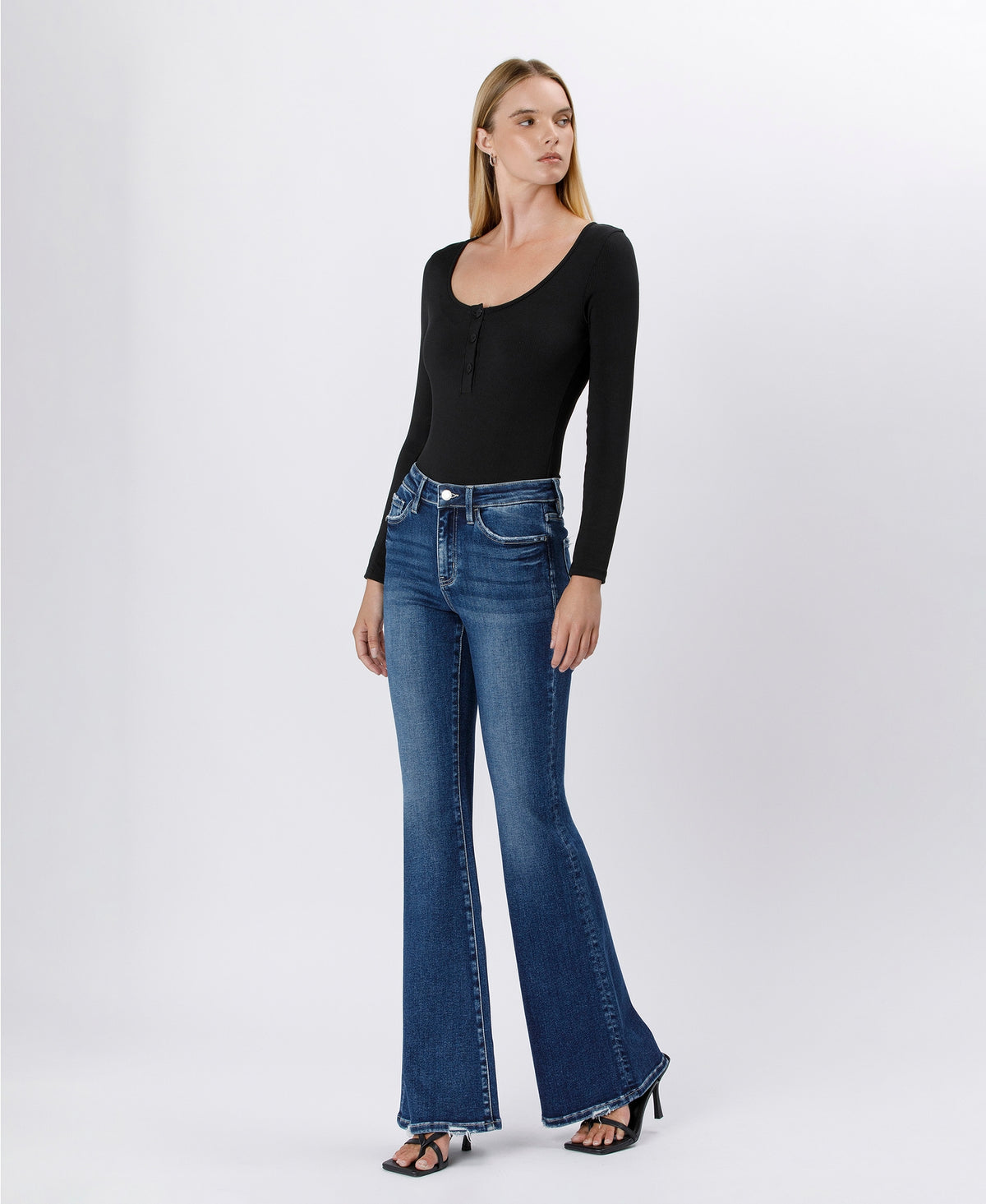 A woman modeling a black long-sleeve scoop-neck top and blue flare jeans against a light gray studio background.