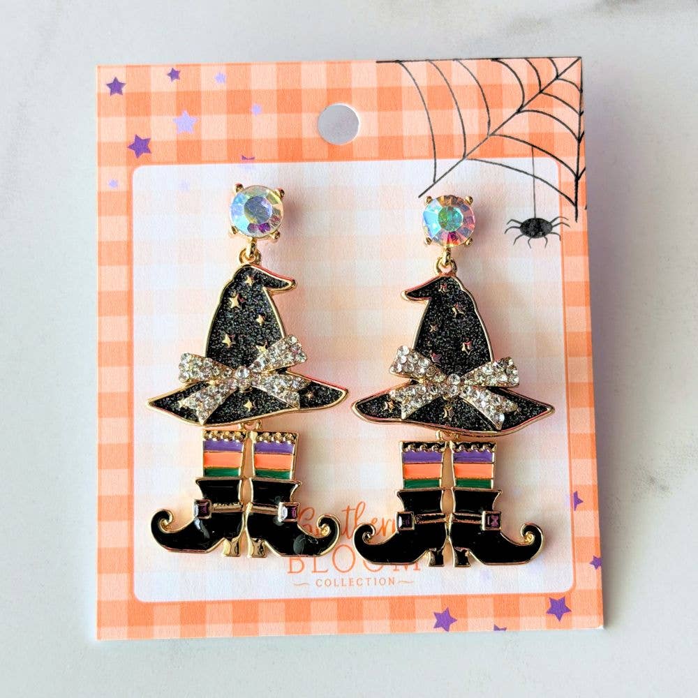 A pair of witch hats displayed on a gingham retail card. The pins feature black glittery witch hats with gold trim, a rhinestone-embellished bow, and striped socks.