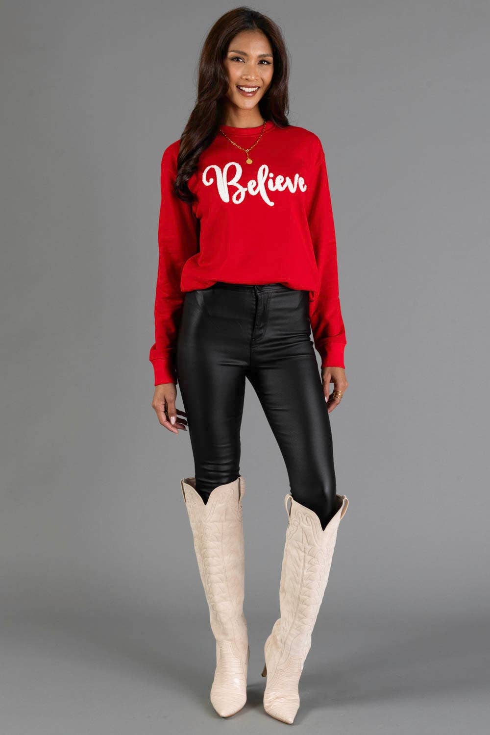 Red Believe sweatshirt styled with black faux leather pants and cream boots