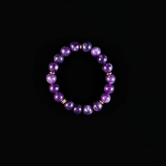 A beaded stretch bracelet made of polished purple amethyst beads separated by small gold spacer rings, displayed against a solid black background.