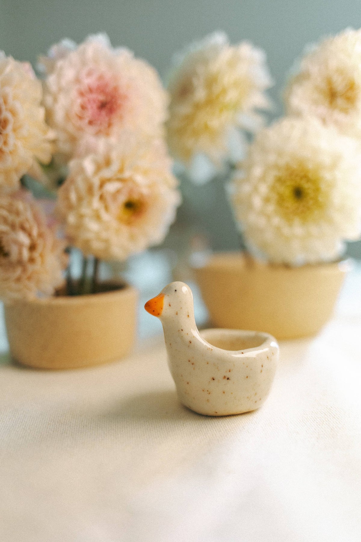 Goose ring dish on a table beside pots of pink dahlias
