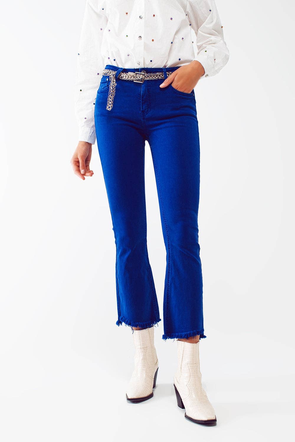 Person wearing blue jeans with a decorative belt and white boots on a white background