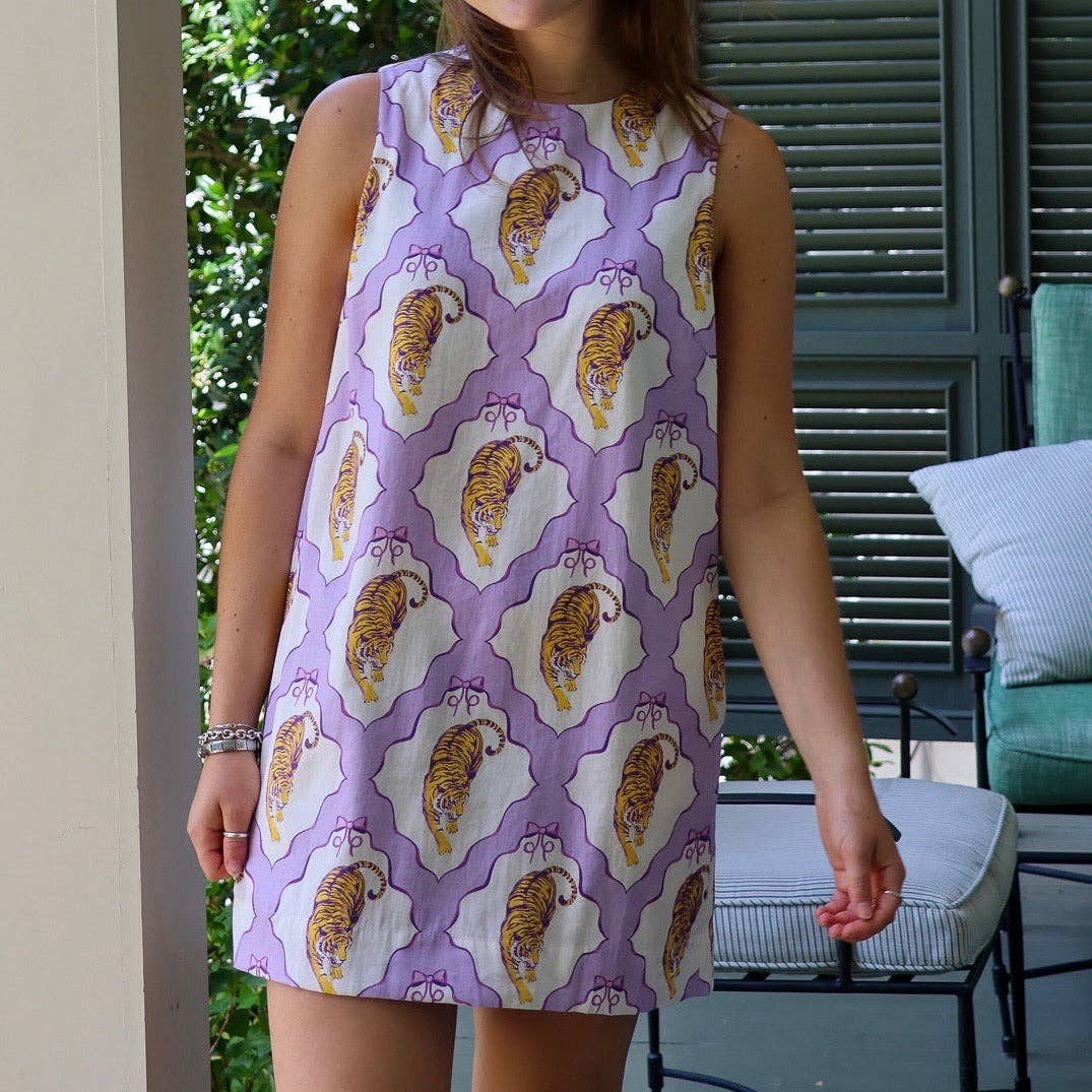 A sleeveless white dress with a purple trellis pattern and orange-and-yellow tiger print, worn by a model on a porch with patio furniture in the background.