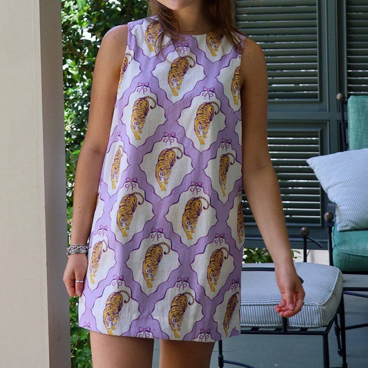 A sleeveless white dress with a purple trellis pattern and orange-and-yellow tiger print, worn by a model on a porch with patio furniture in the background.
