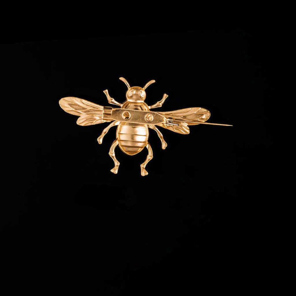 A polished gold bee brooch with detailed wings and legs, shown against a solid black background.