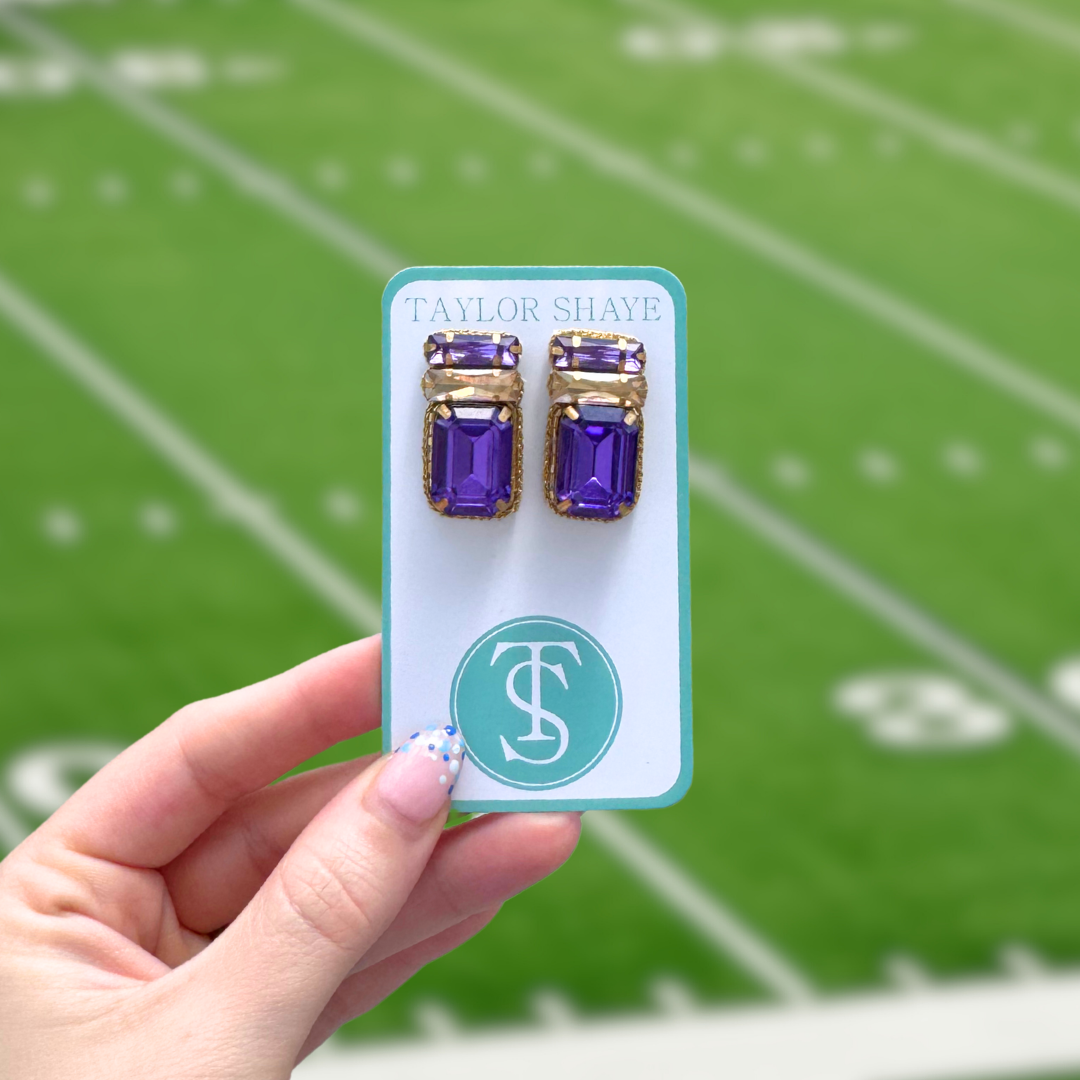 Purple and gold earrings on a Taylor Shaye card held against a football field background