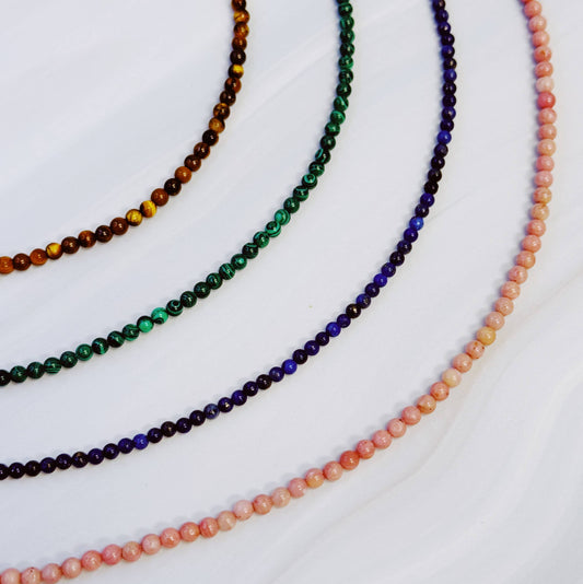 Four beaded necklaces in different colors on a white background