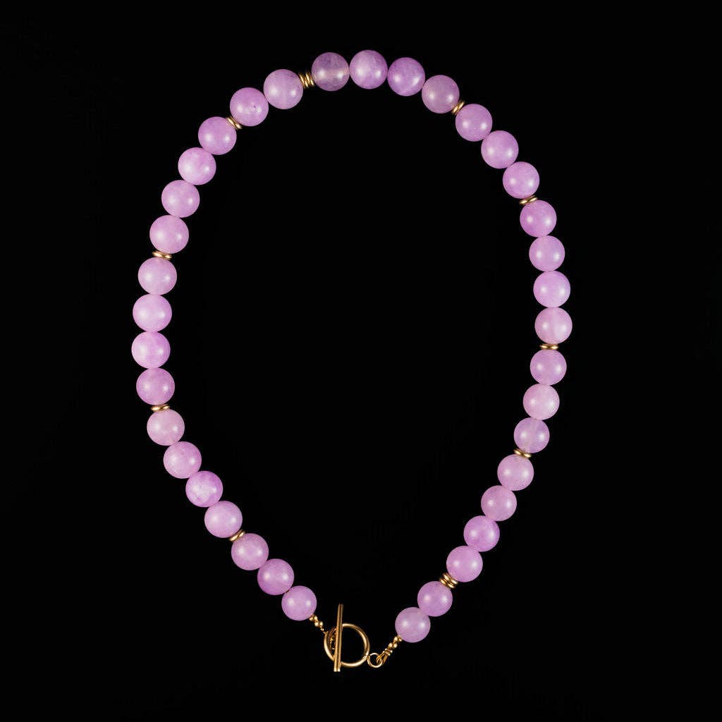 A beaded necklace made of smooth, round light purple beads separated by small gold spacer beads, finished with a gold toggle clasp, displayed on a solid black background.