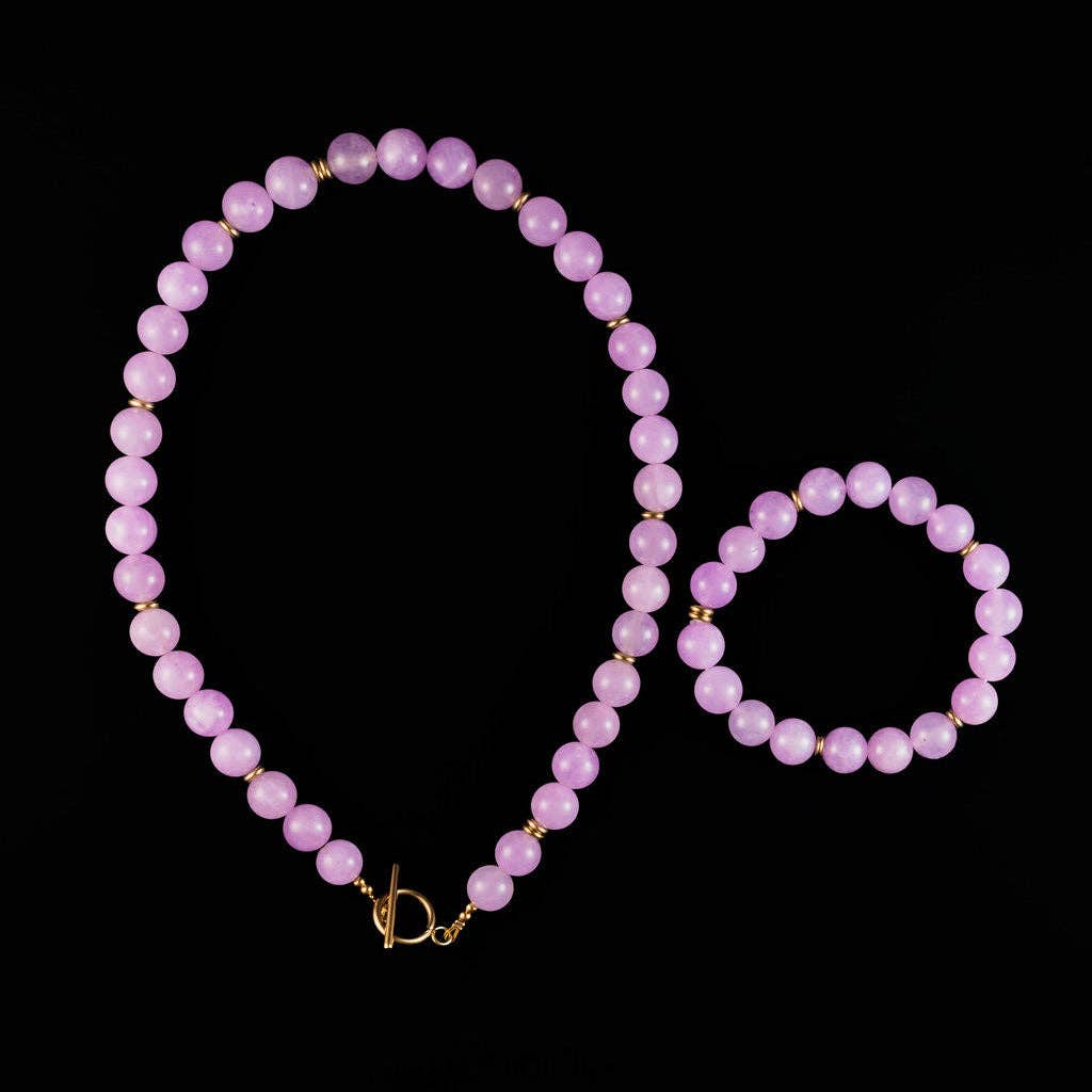 A matching beaded necklace and bracelet set in light purple/lavender beads with small gold spacer accents, displayed on a solid black background.