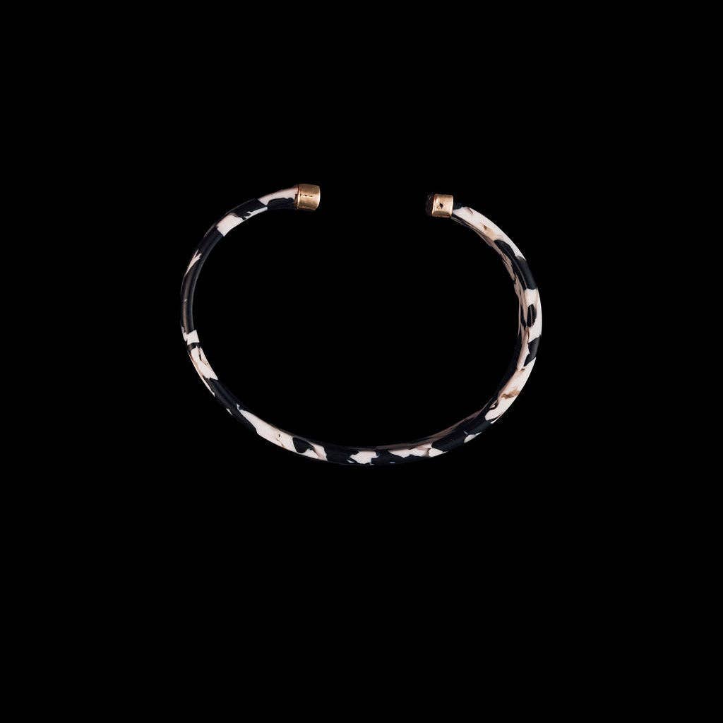 A thin open cuff bracelet with a black and white leopard print pattern and gold-toned metal ends, shown against a solid black background.