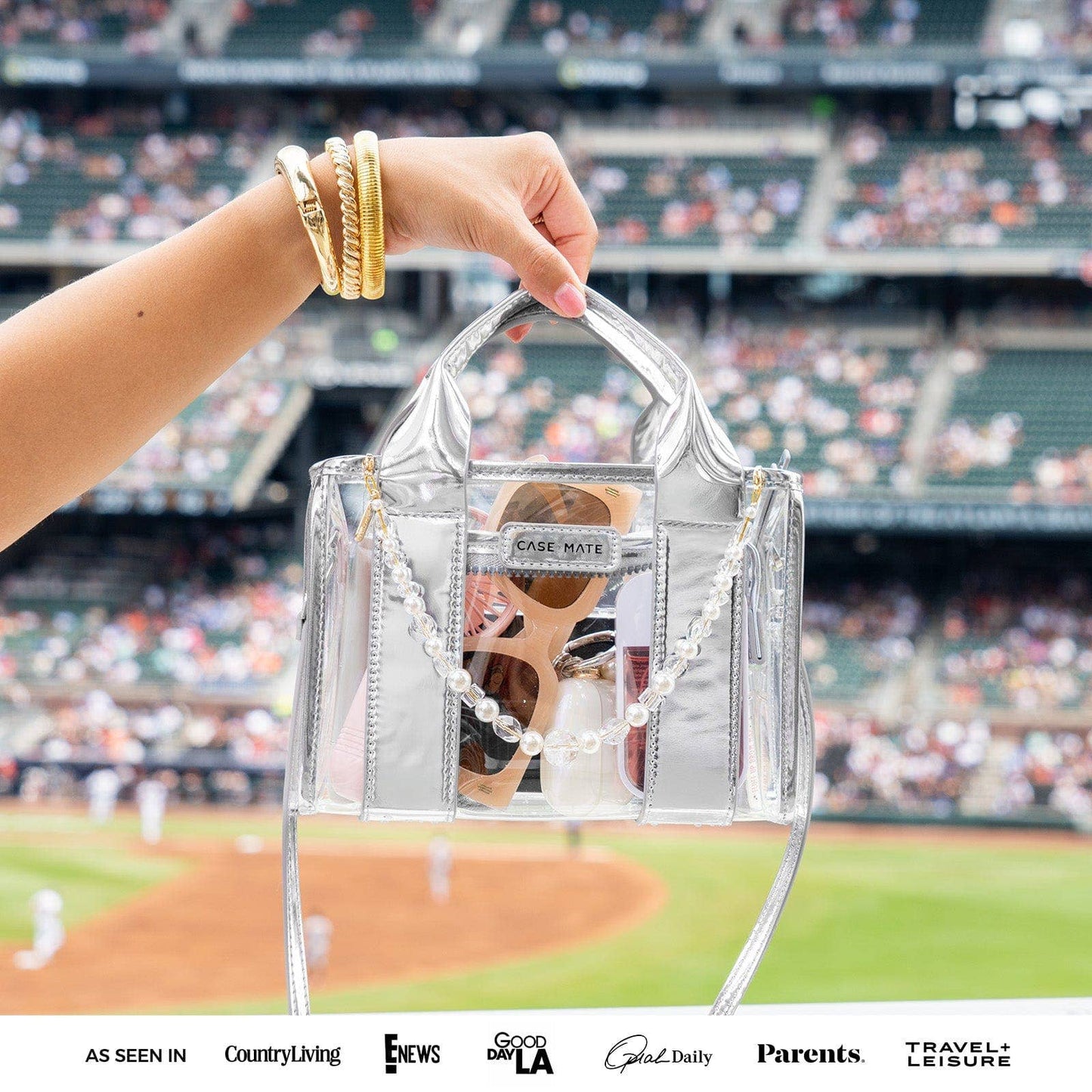 Clear handbag with sunglasses held by a hand at a baseball game.
