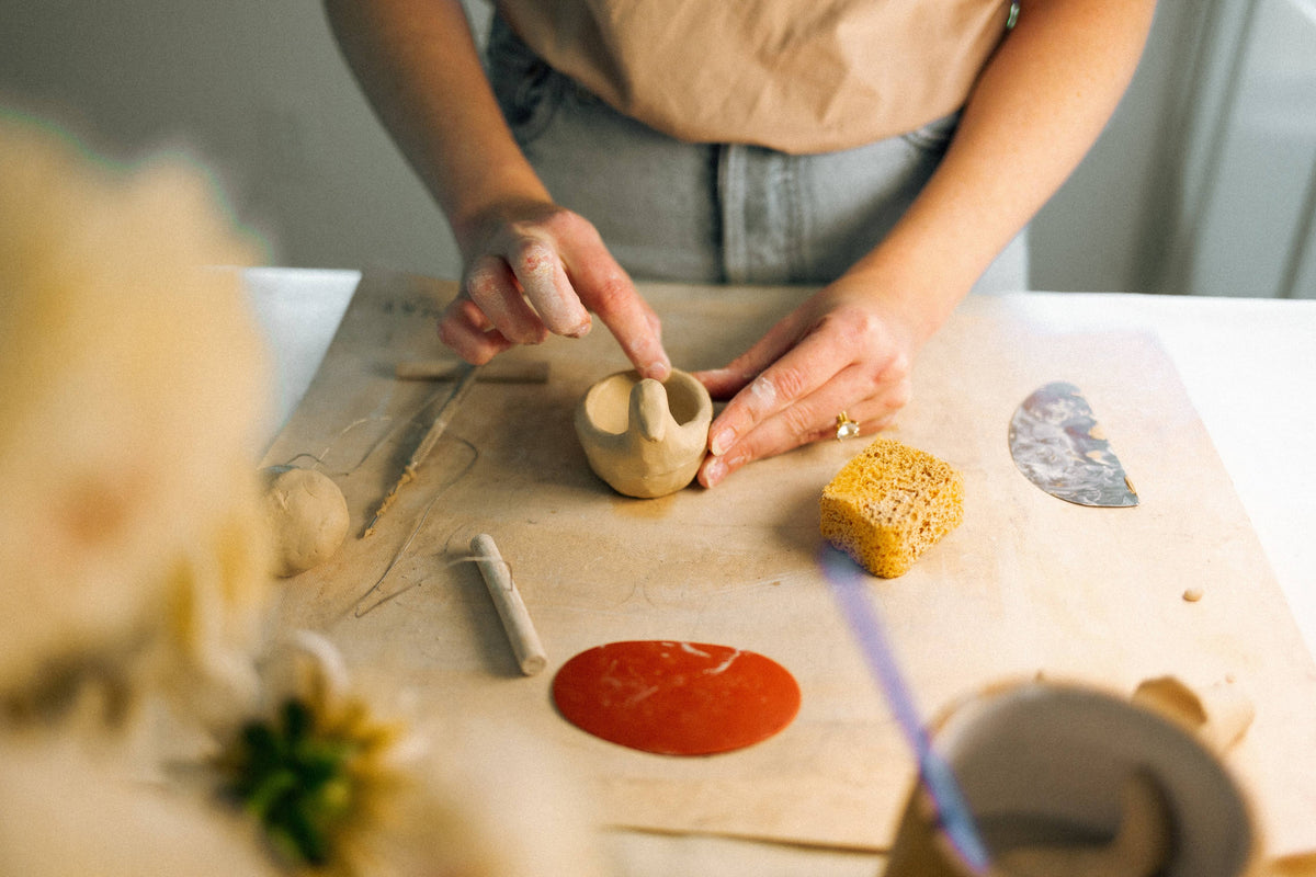Artist's hands shaping clay for a goose ring dish on a work table