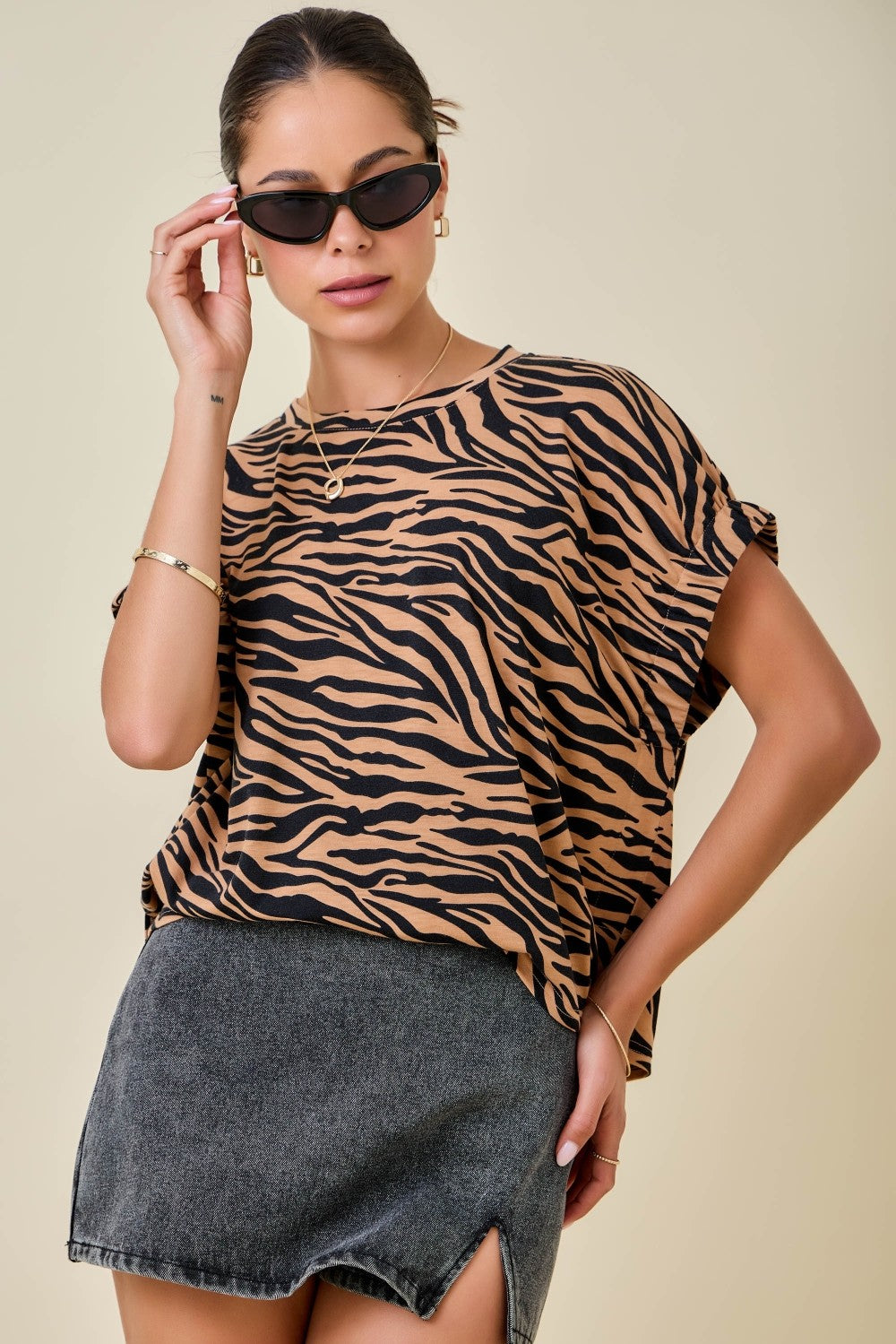 Woman wearing a tiger print top and denim skirt on a beige background