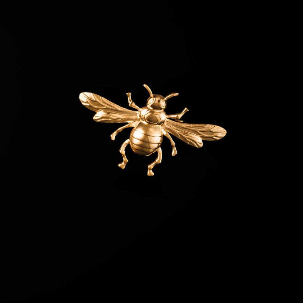 A polished gold bee-shaped brooch or pin, shown in profile against a solid black background.