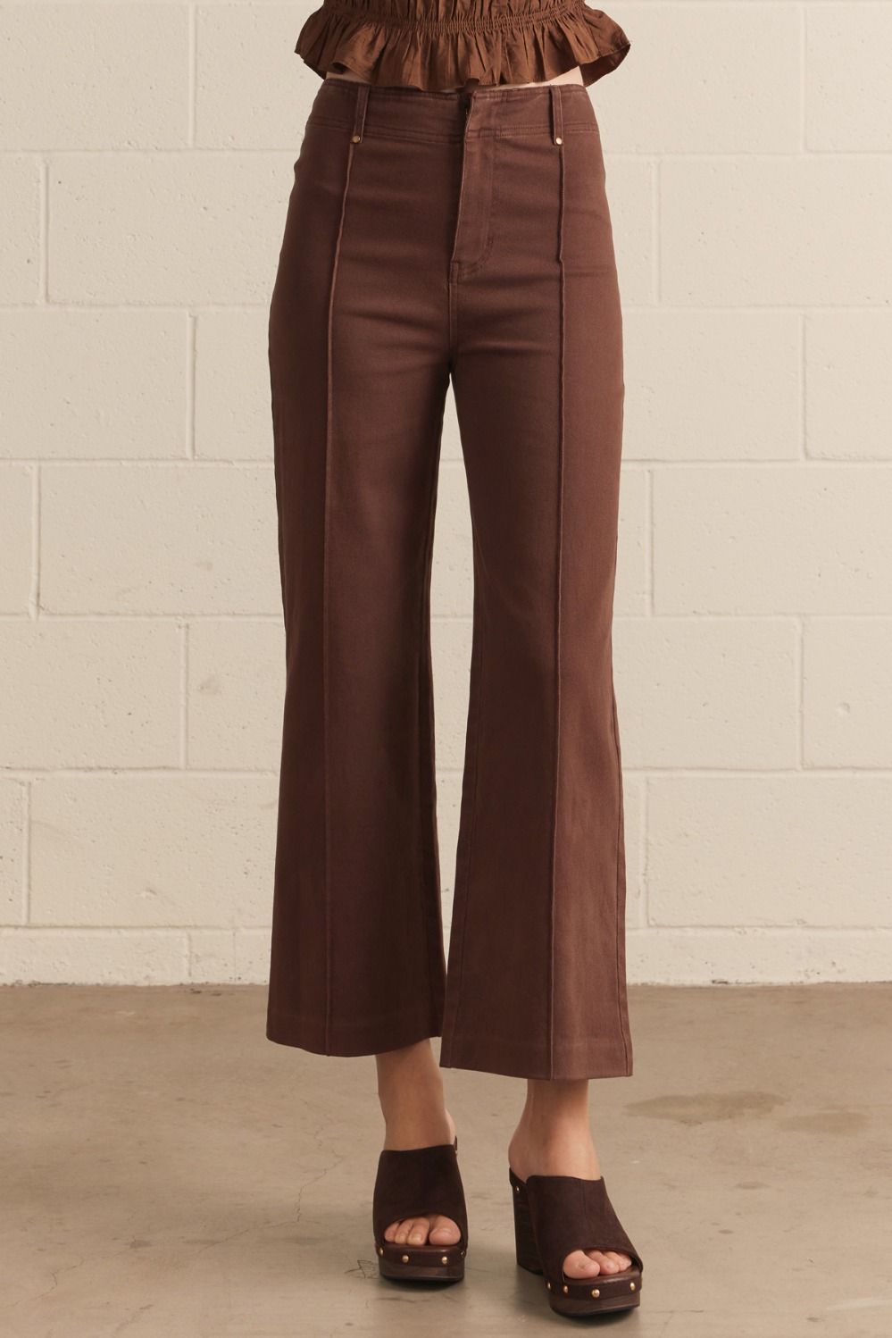 Brown pants worn by a person against a beige brick wall.