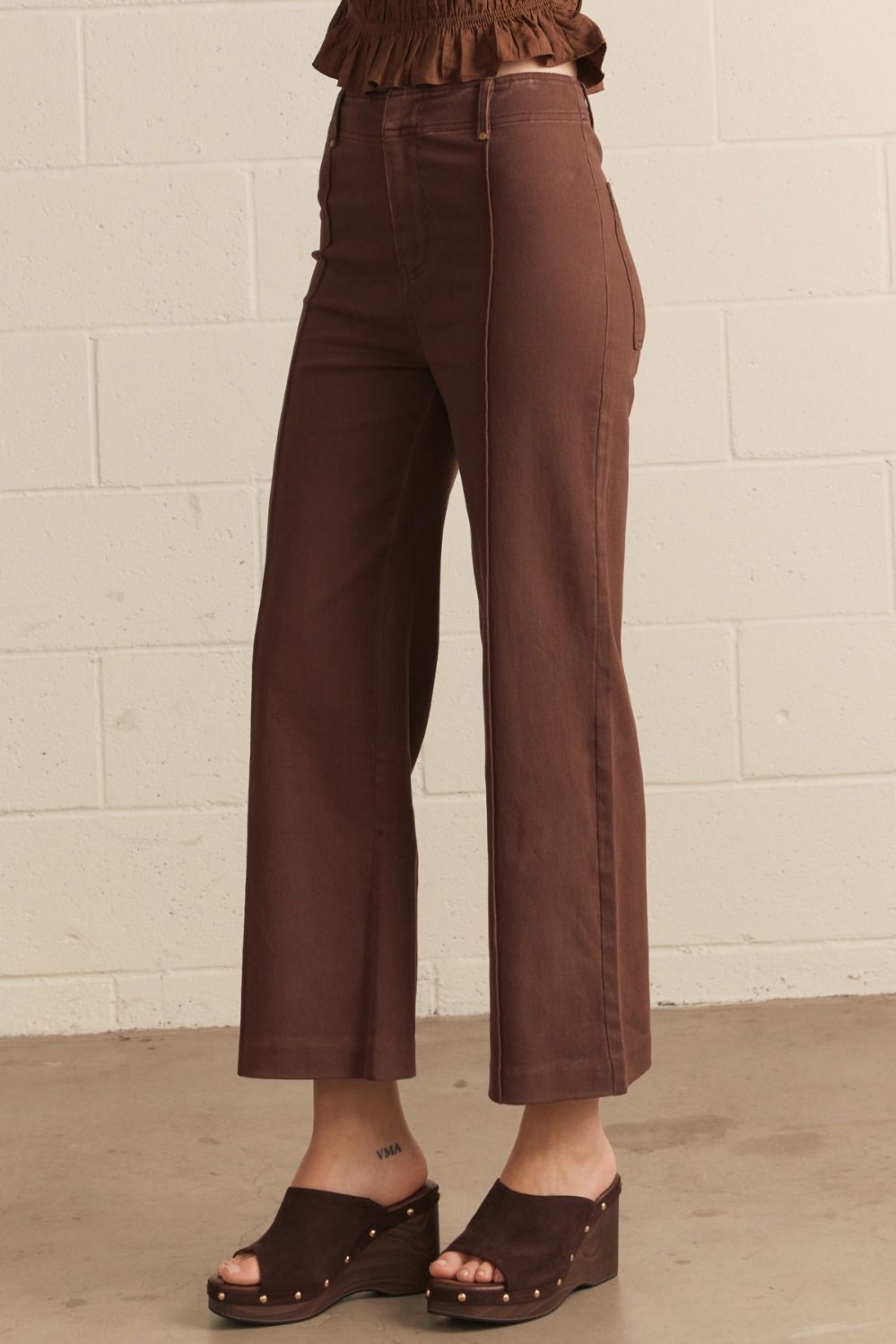 Person wearing brown pants and sandals against a white brick wall.