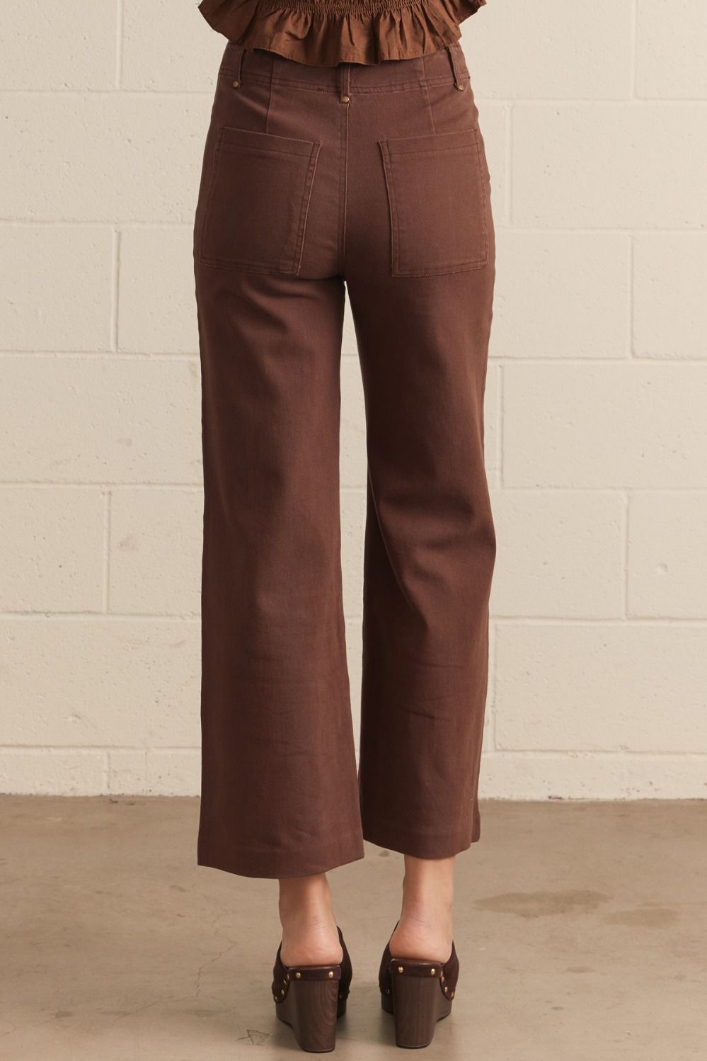 Brown pants worn by a person against a beige brick wall.