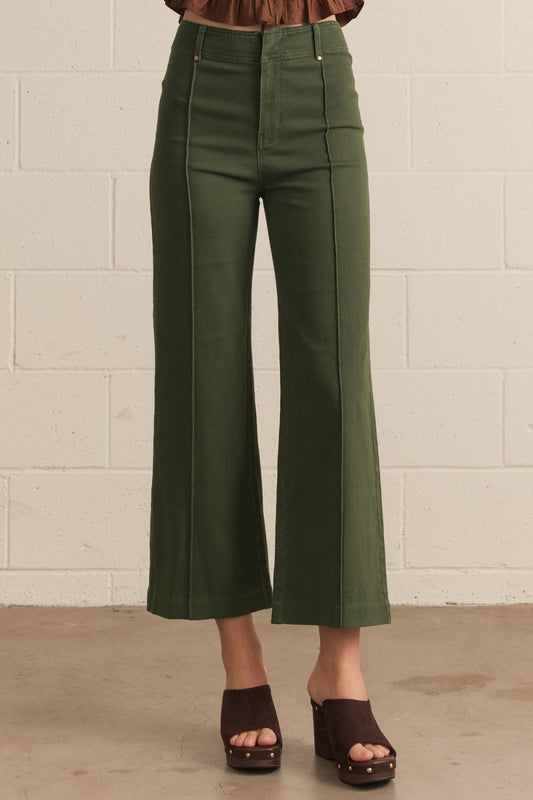 Person wearing hunter green pants with front seam detail against a white brick wall.