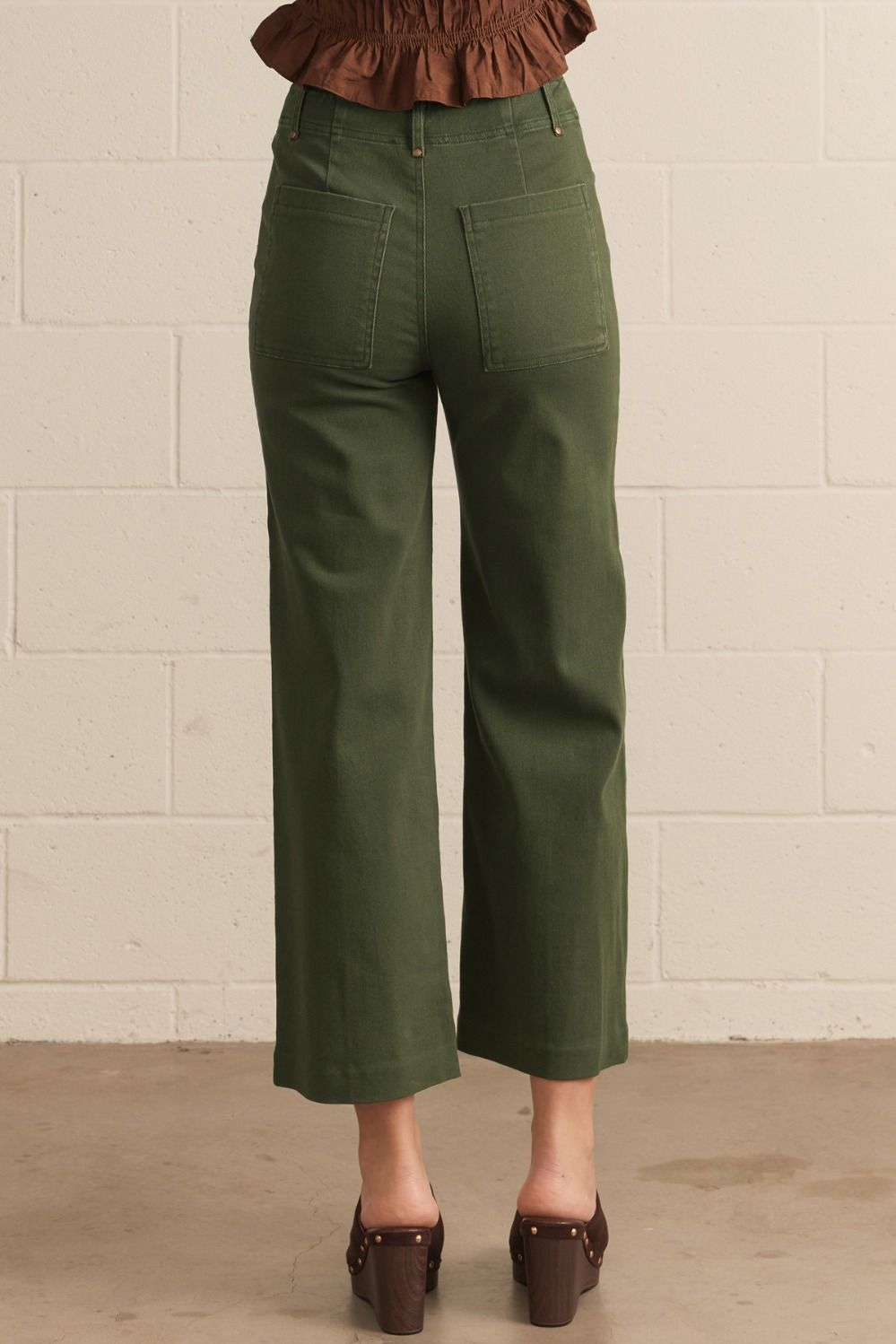 Hunter Green pants worn by a person against a beige brick wall.
