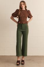 A woman modeling a brown smocked puff-sleeve crop top and hunter  green cropped wide-leg pants, standing against a light beige brick wall.