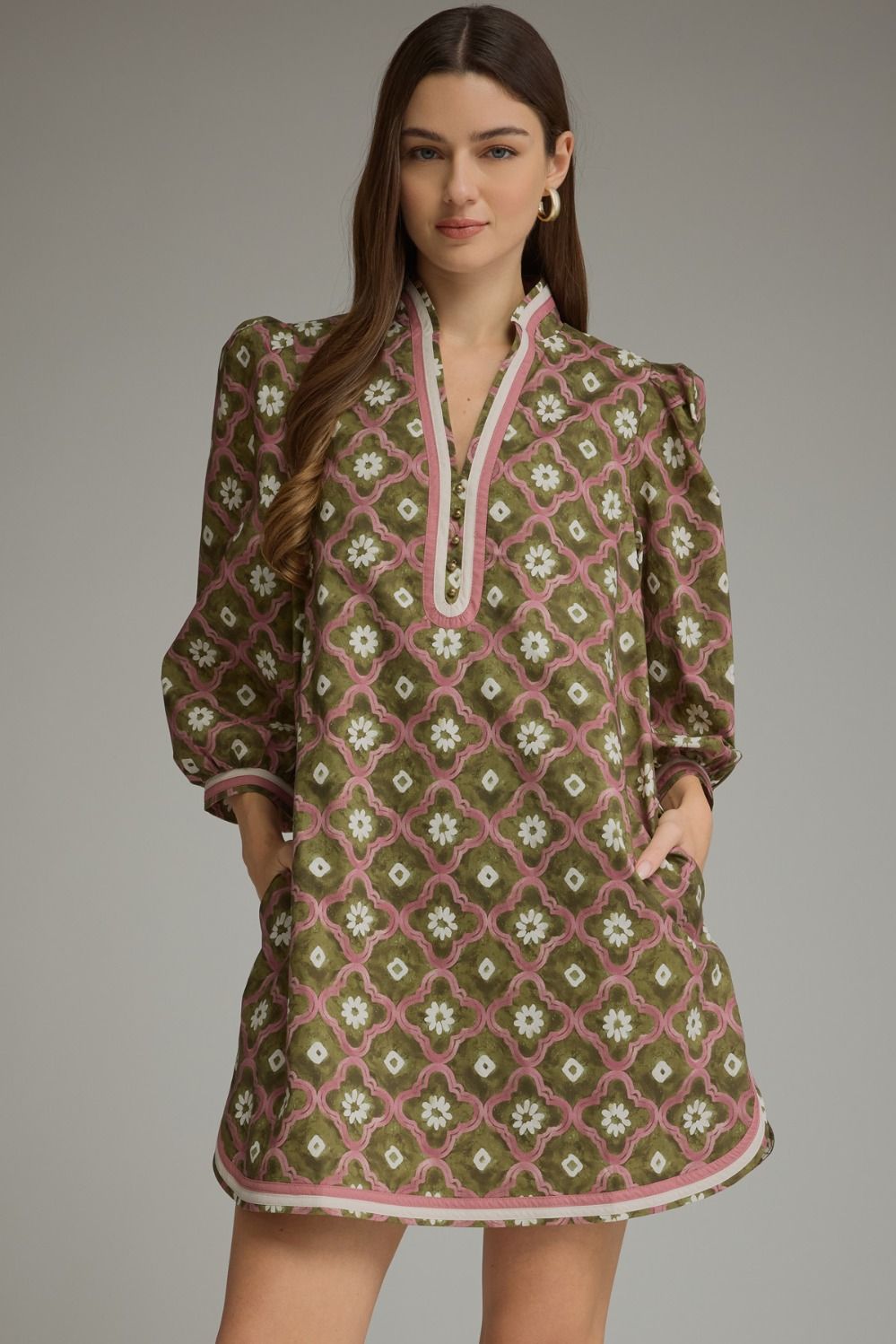 A woman modeling a brown and pink patterned dress with white floral details, set against a solid gray studio background.