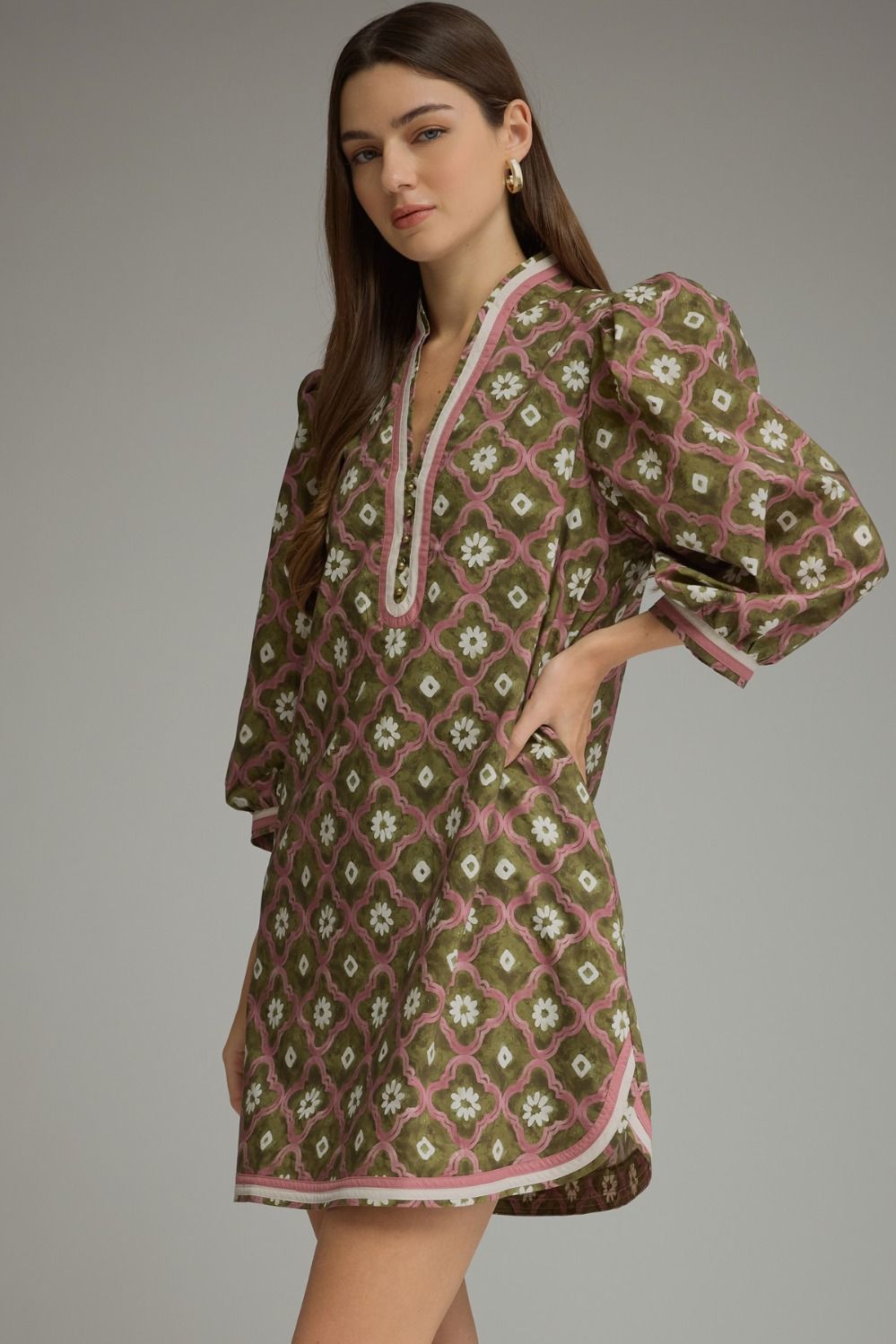 A woman modeling a short, loose-fitting tunic dress with a brown, pink, and white geometric floral pattern, featuring puff sleeves and a split neckline.