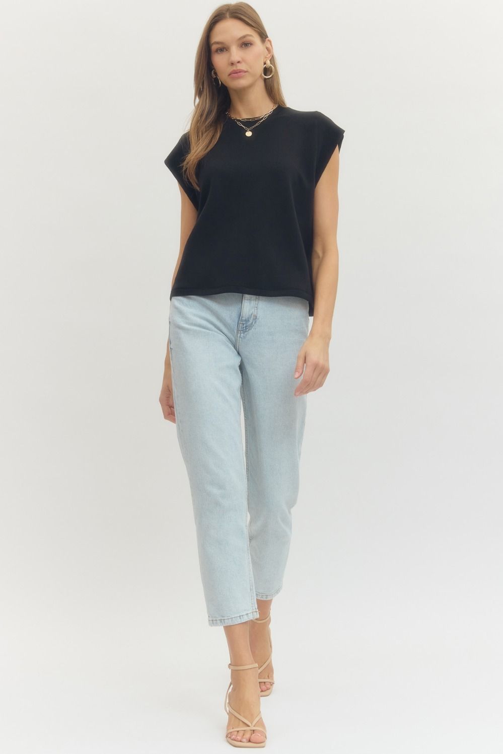Woman wearing a black cap sleeve top and light blue jeans on a white background