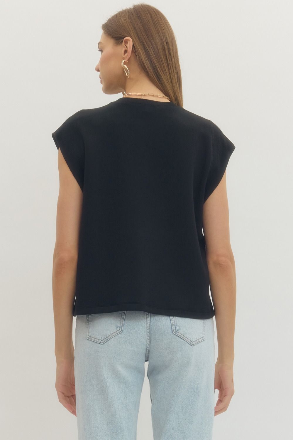 Person wearing a black  cap sleeve top and light blue jeans on a white background