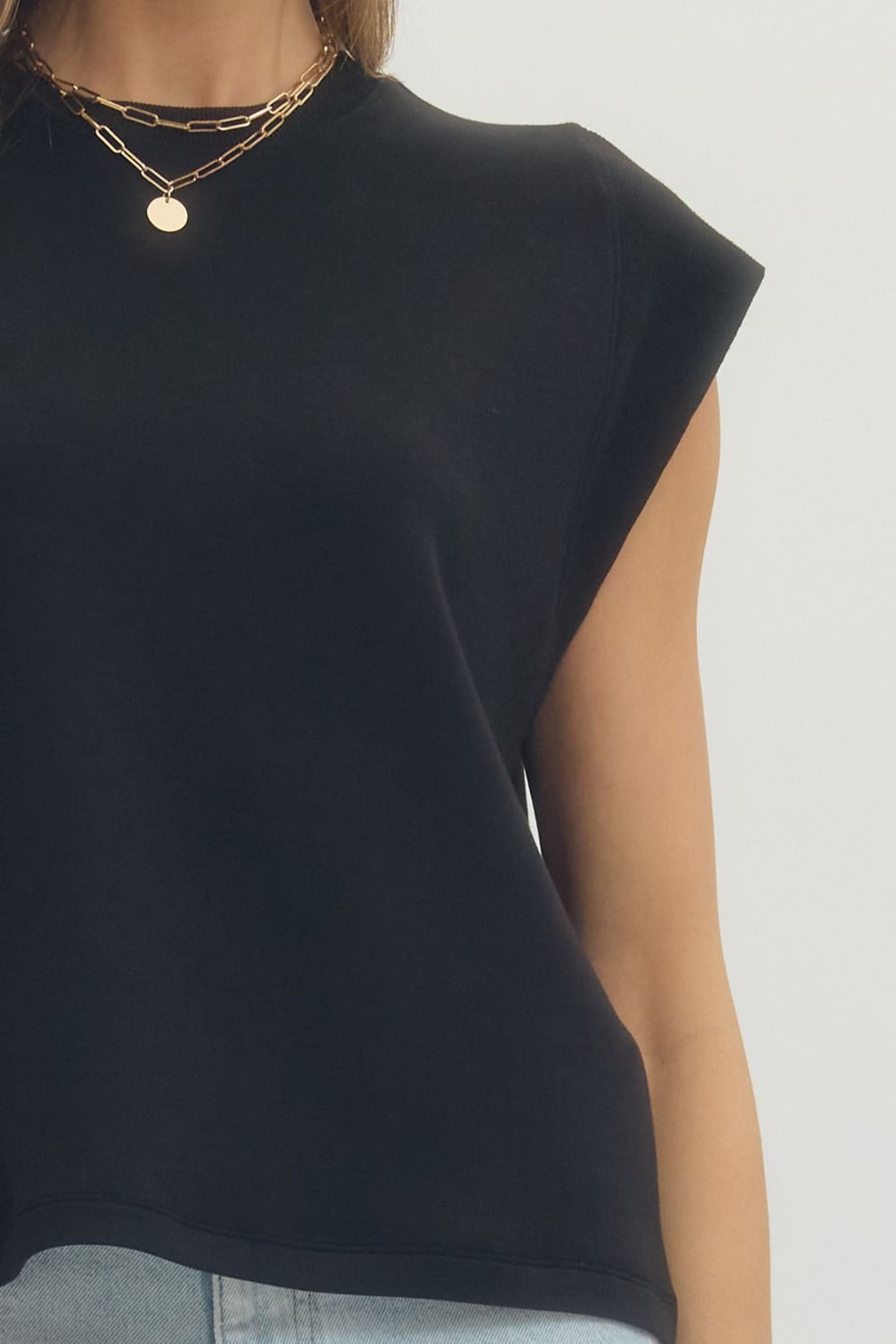 Black cap sleeve top worn by a person on a plain background