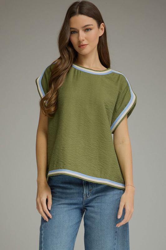 A woman wearing a short-sleeve olive green top with light blue and white striped trim, paired with blue jeans, against a neutral gray studio background.