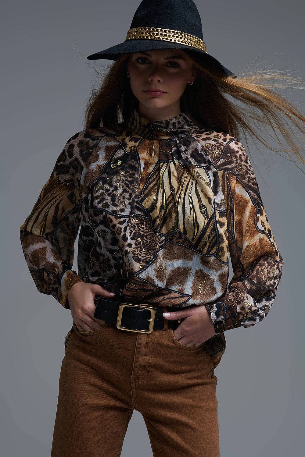 Person wearing a patterned blouse and brown pants with a dark background