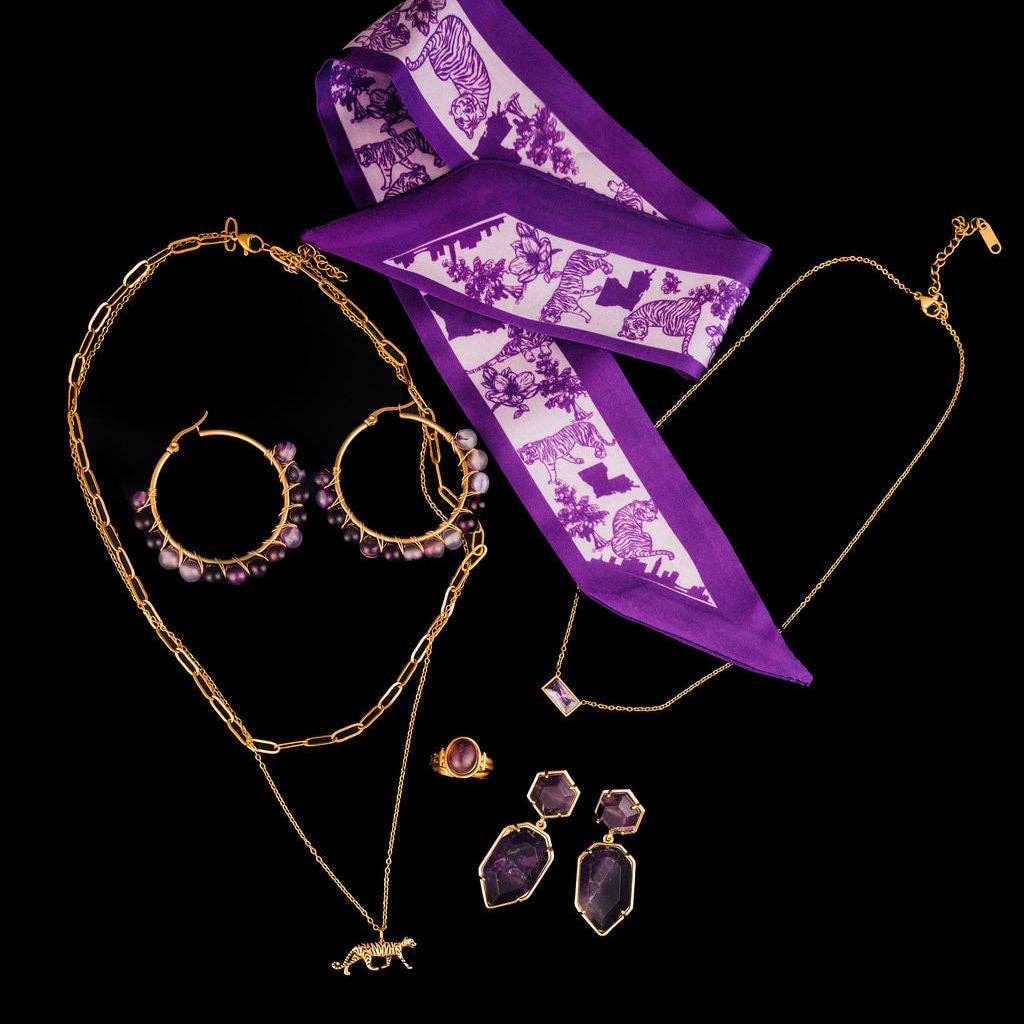 A jewelry set featuring gold-tone chains, hoop earrings with purple beads, a necklace with a horse charm, matching purple gemstone drop earrings, and a purple-and-white patterned silk scarf, arranged on a solid black background.