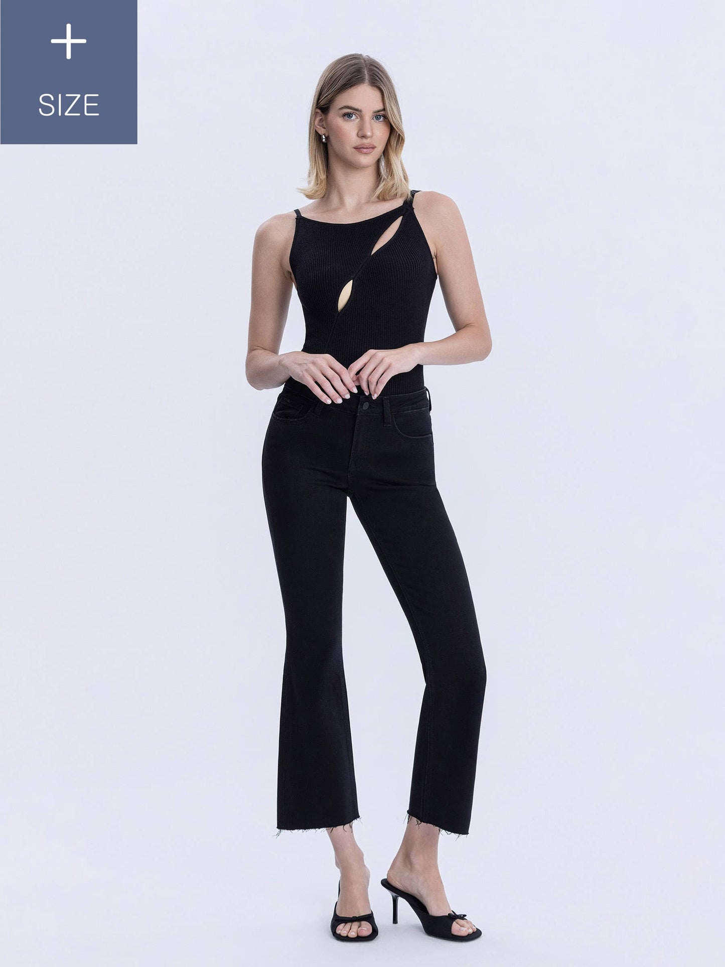 A woman modeling a black sleeveless top with cutout details and black cropped flare pants against a light gray studio background. Plus size notice in top left corner