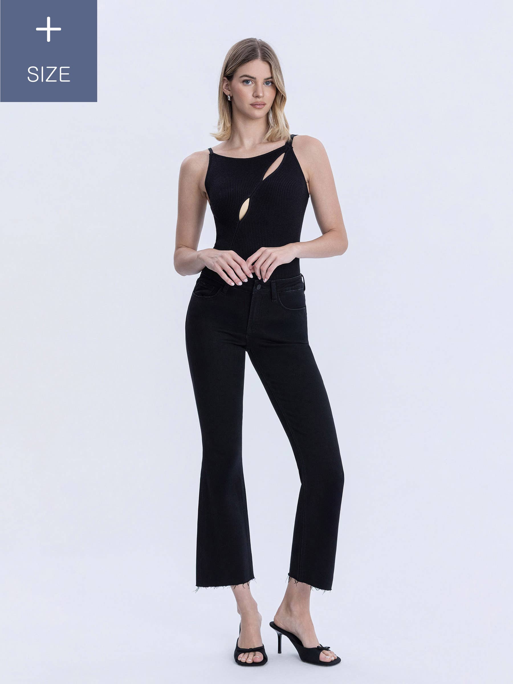 A woman modeling a black sleeveless top with cutout details and black cropped flare pants against a light gray studio background. Plus size notice in top left corner