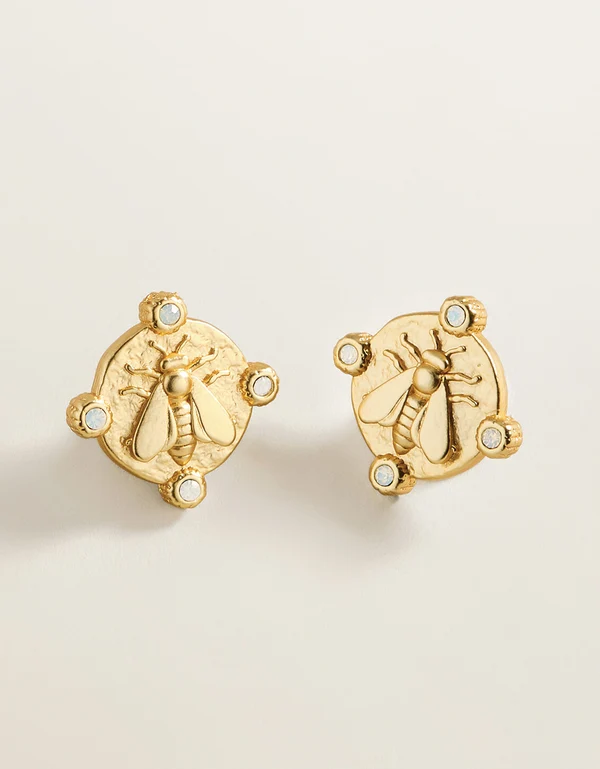 A pair of gold bee stud earrings with small clear rhinestone accents, displayed on a clean, light beige background.