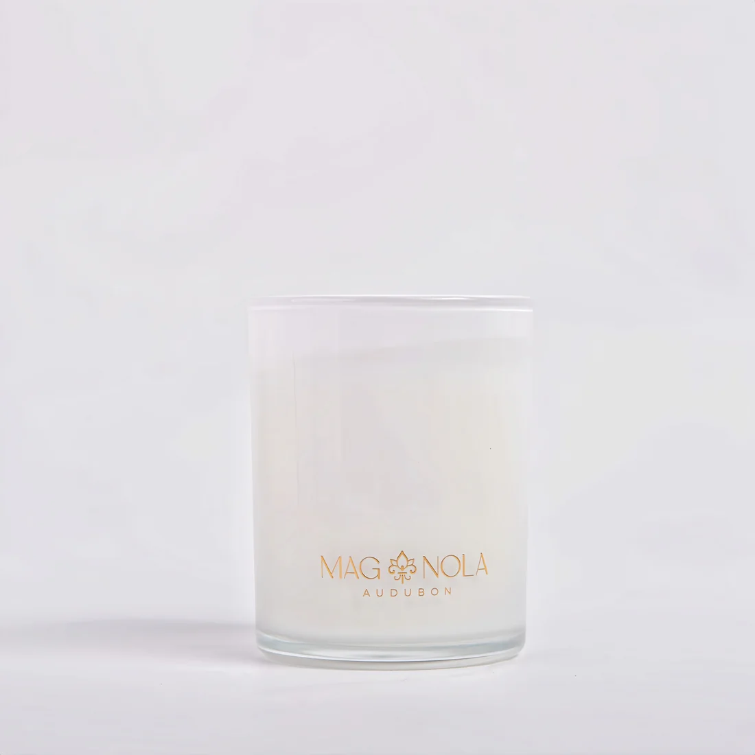 A frosted 8.5 oz glass jar candle with white wax and gold lettering that reads 'MAG NOLA AUDUBON' on a clean white background.