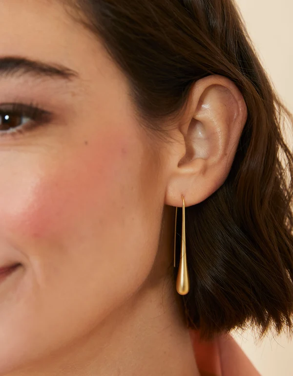 Close-up of a woman wearing a gold earring with a neutral background