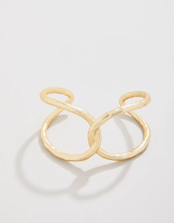 A gold-colored, twisted infinity-style ring with a hammered texture, resting on a light surface.