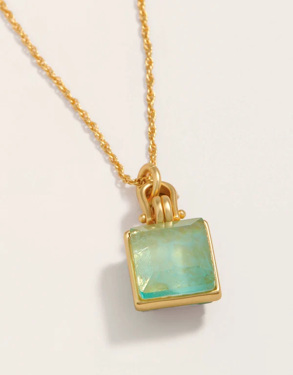 A gold chain necklace with a square pendant featuring a light green gemstone in a gold bezel setting, shown on a clean off-white background.