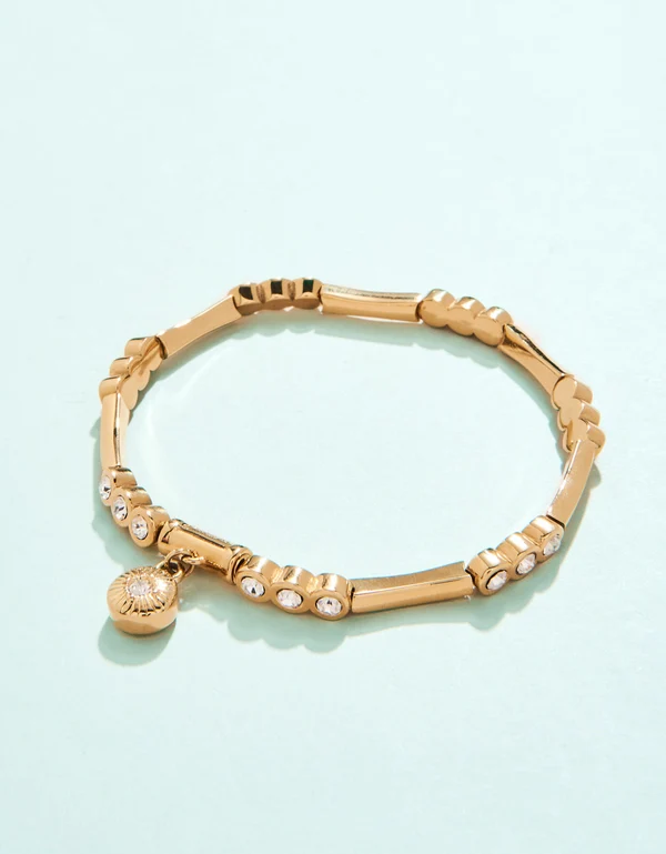Gold stretch bracelet with rhinestone studs and dangle on a white background. 