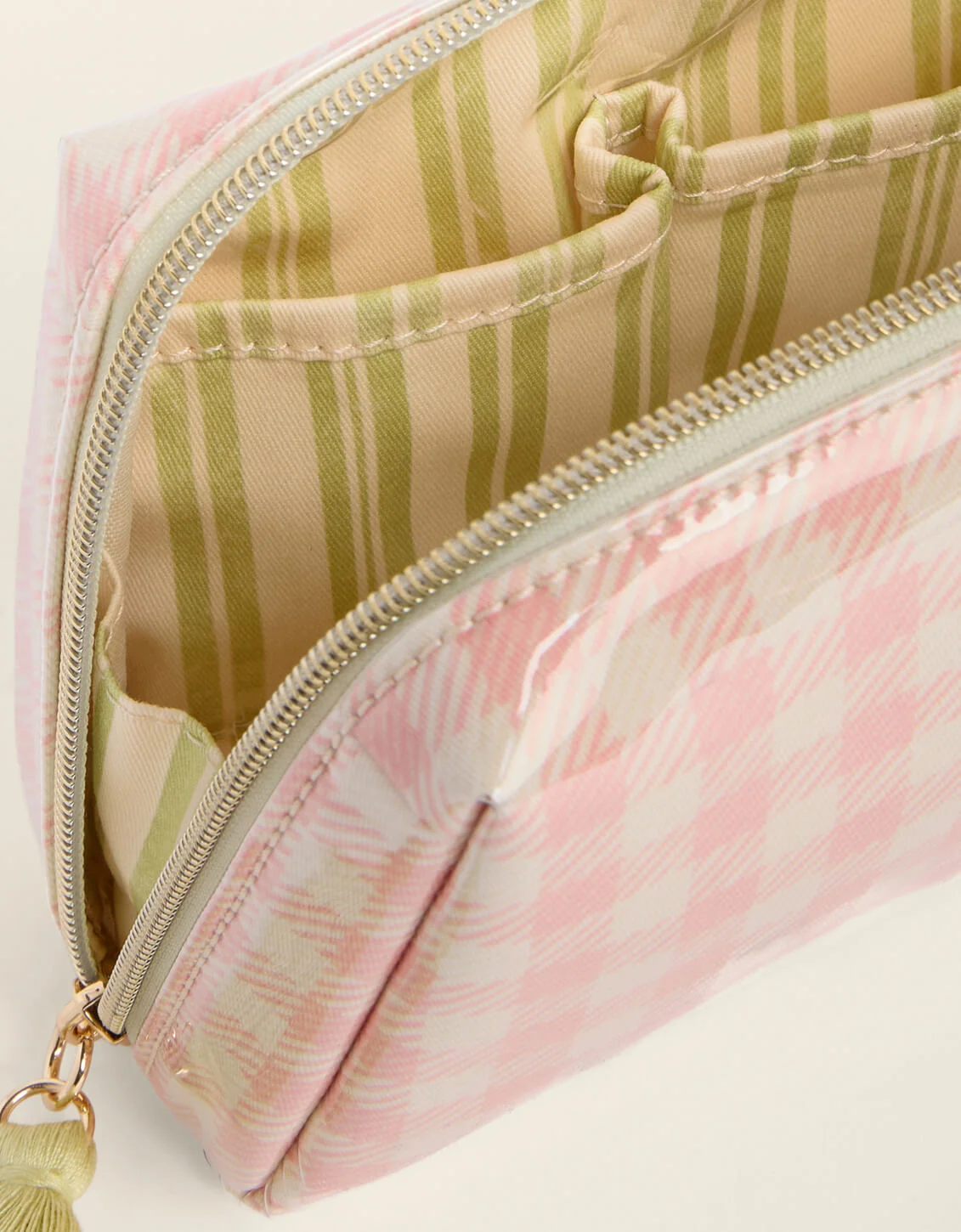 Close-up of a zippered cosmetic pouch with a pink and white patterned exterior and a beige interior featuring olive green stripes.