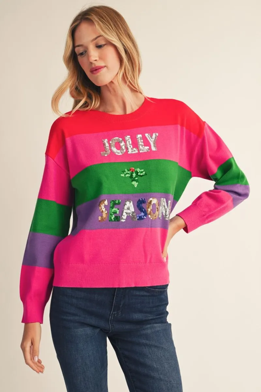 Woman in a multicolor striped crewneck sweater with sequin JOLLY SEASON lettering, worn with dark jeans