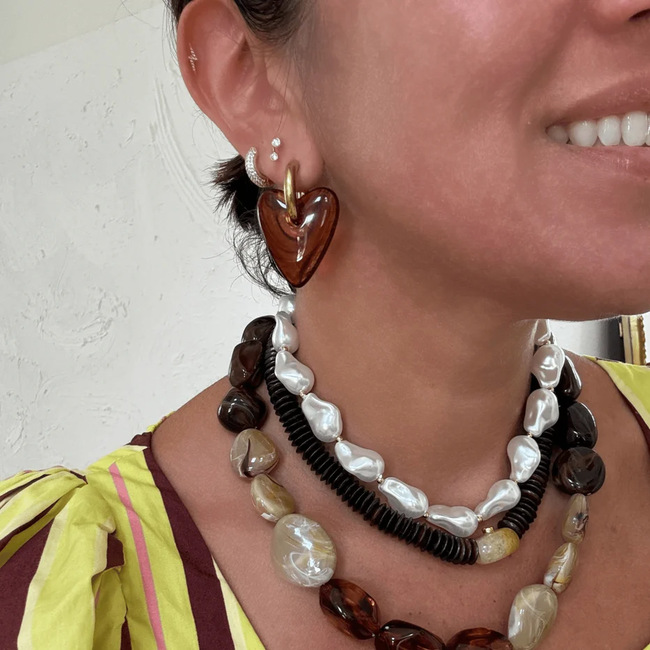 Close-up of a person wearing a heart-shaped amber glass drop earring with a gold ring.